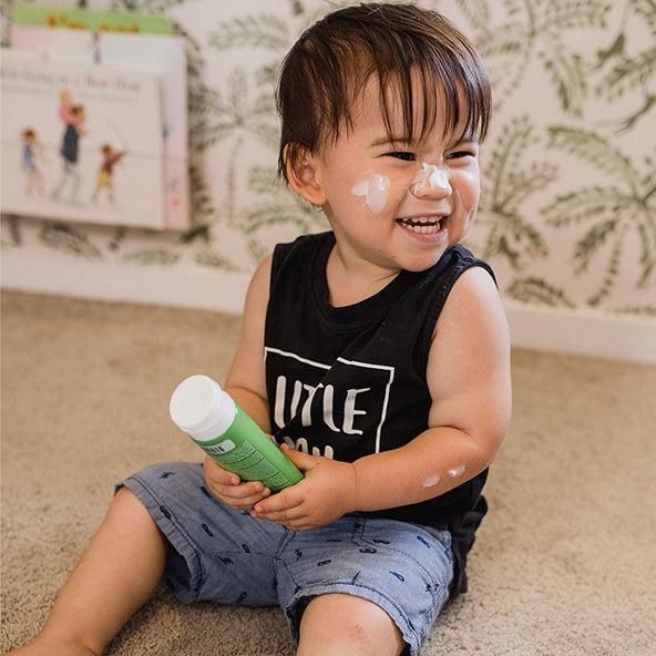 Smiling toddler with MooGoo Baby & Child Soothing Moisturiser Nut Oil Free, playful cream on face and arms, paediatrician approved natural nut free to calm redness and dryness in the skin.