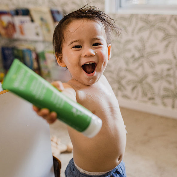 Smiling toddler with MooGoo Baby & Child Soothing Moisturiser Nut Oil Free, playful cream on face and arms, paediatrician approved natural nut free to calm redness and dryness in the skin.