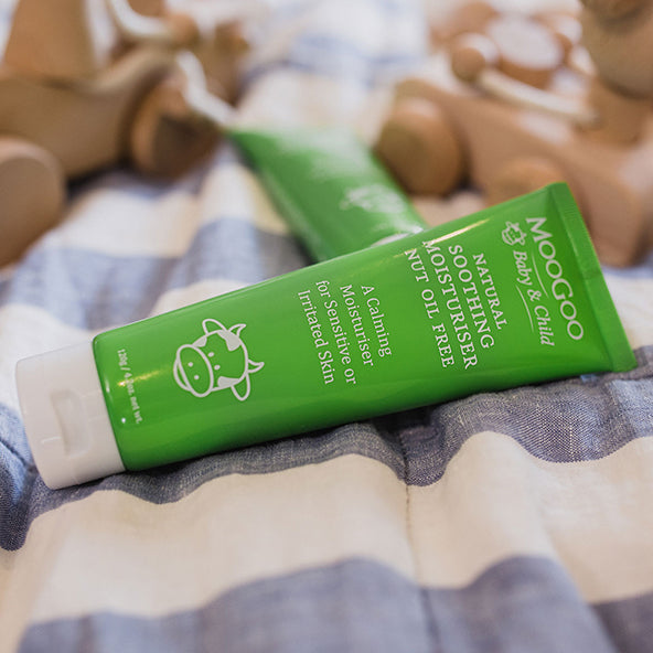 MooGoo Soothing Moisturiser Nut Oil Free tube on soft fabric with toys in background, natural nut-free cream safe for delicate baby and child skin