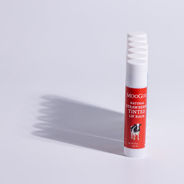 Straight line of MooGoo Strawberry Tinted Lip Balm  white background, natural lip care with edible oils, soft hydration and a gentle strawberry flavour, phthalate free, petroleum free, beetle and synthetic dye free. 