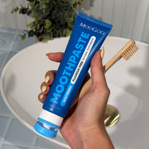 MooGoo Fluoride-Free Peppermint Whitening toothpaste tube with toothpaste being squeezed out, held by a hand.