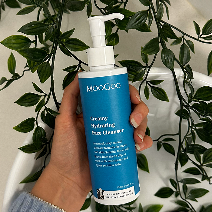  MooGoo Creamy Hydrating Face Cleanser 250ml held against leafy background, A natural, silky smooth cleanser formula for soft skin.